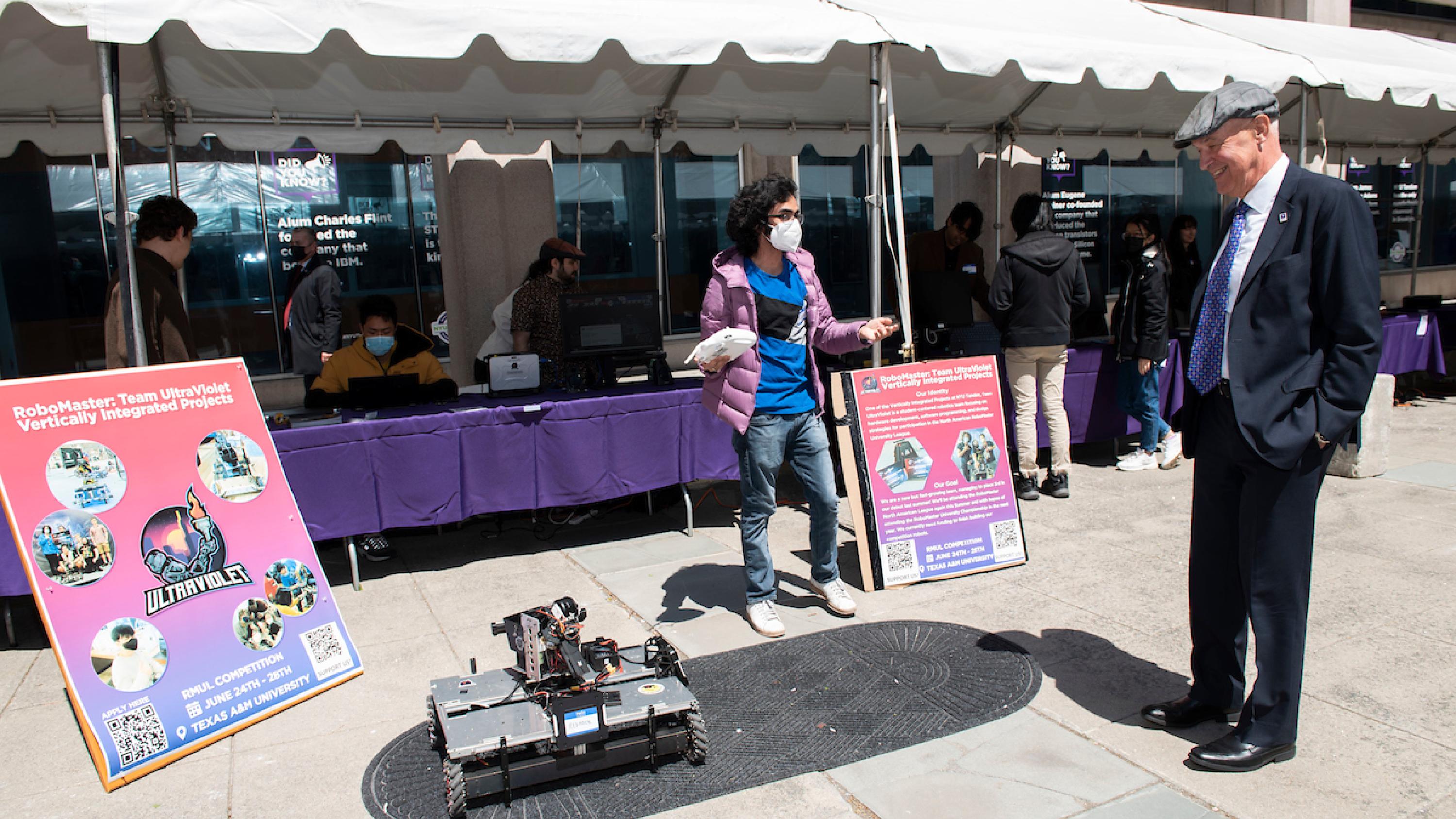 A student on the NYU RoboMaster Team UltraViolet, a Vertically Integrated Project, demonstrates a rover as NYU President Andrew Hamilton looks on at last year's Research Excellence Exhibit